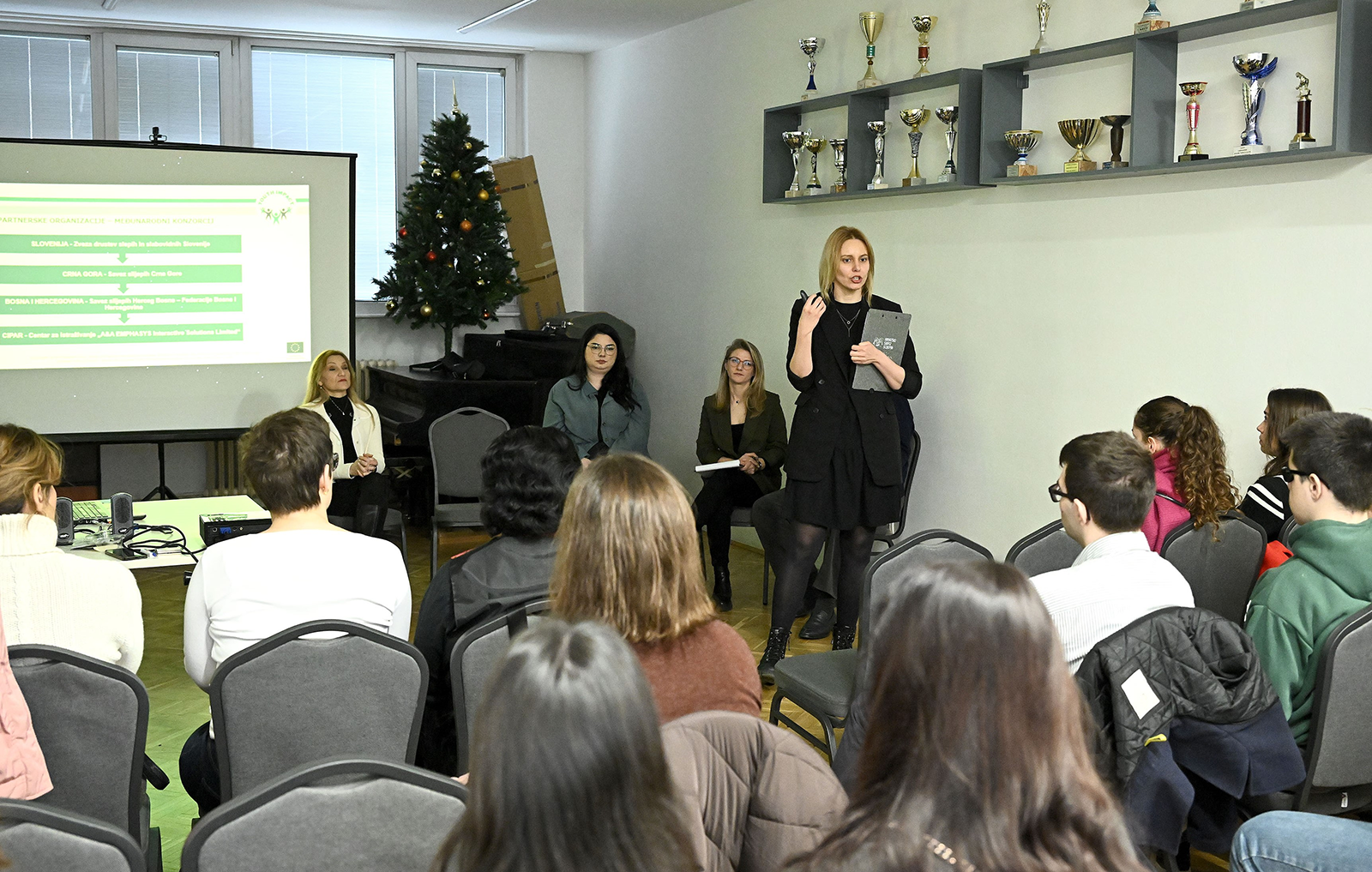 Presenter standing next to a projected presentation, speaking to an audience.