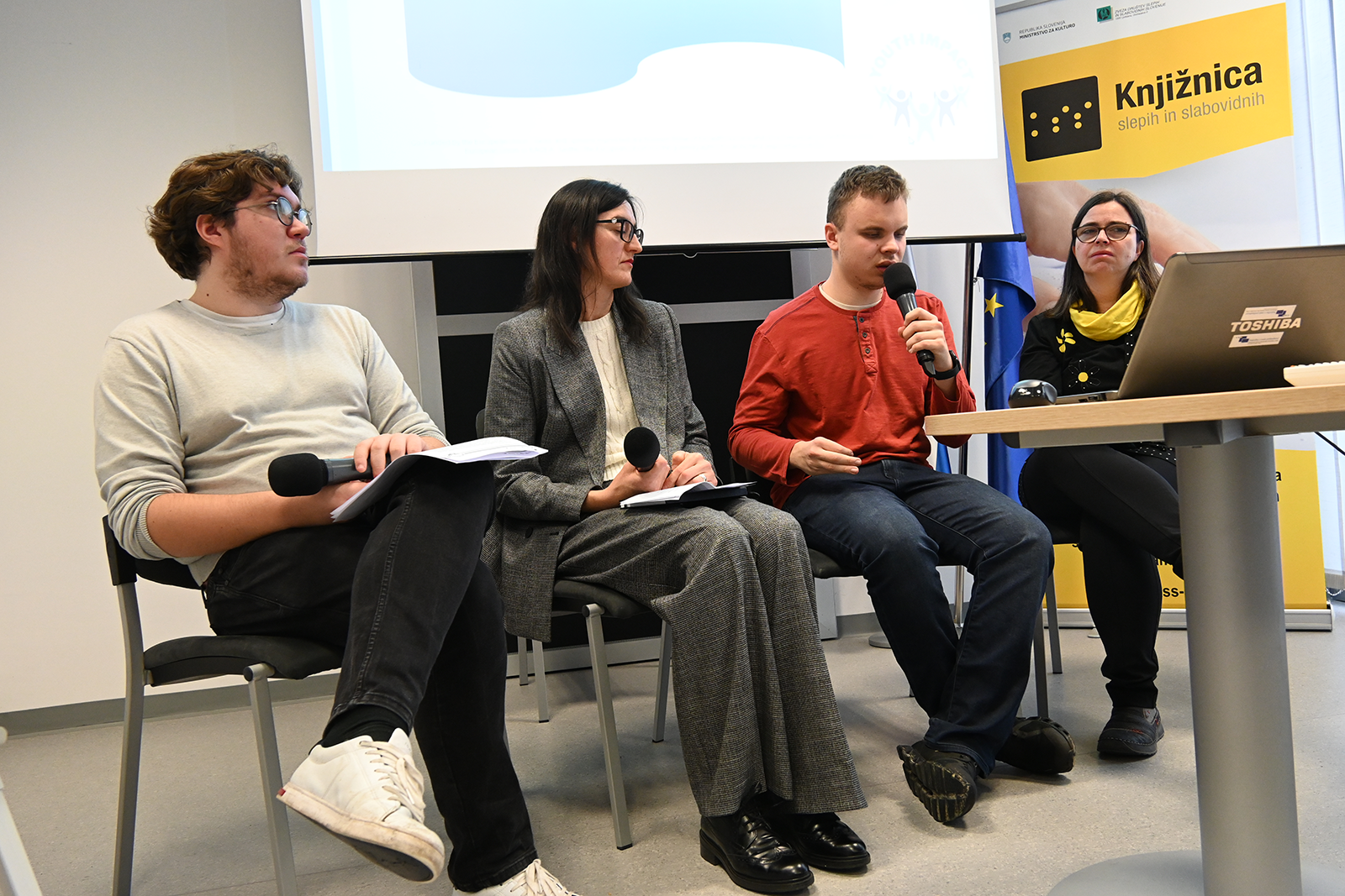 Four panelists sit in a row, speaking during a public discussion.